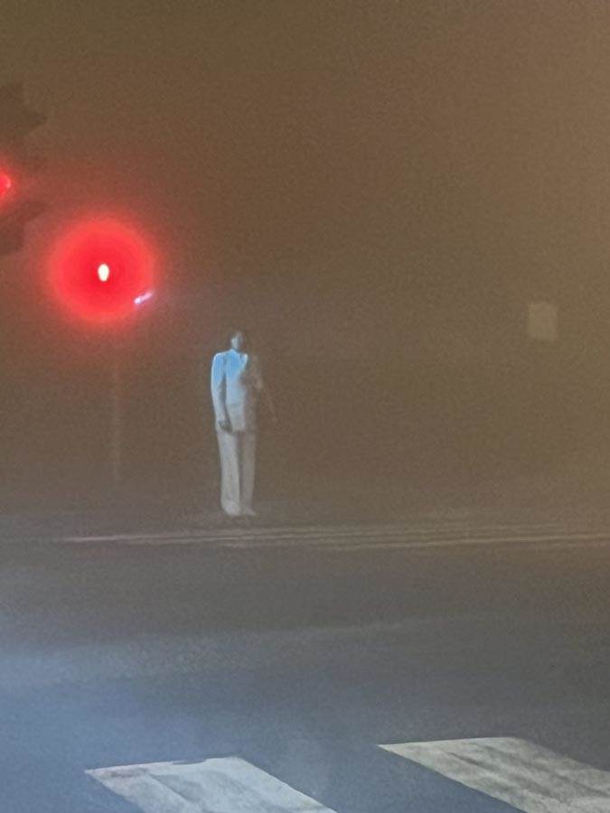  Žena u belom odelu stoji usred noći na semaforu 