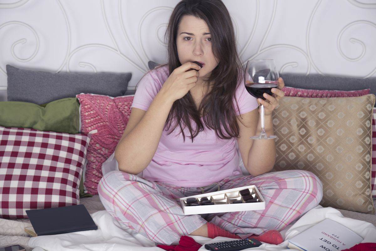  Žena jede čokoladu i pije vino na krevetu 