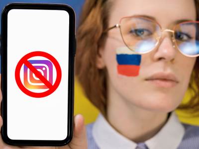  Devojka sa ruskom zastavom na obrazu drži telefon sa precrtanom Instagram ikonicom na ekranu. 